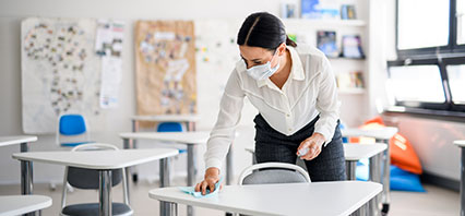 Woman cleaning desks in classroom